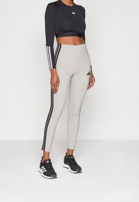 Svart långärmad crop top med vit tre-stripes design; grå högmidjade leggings med svarta sidostråk; svarta sportskor med vit sula.