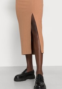 Randig, midilång kjol i ljusbrun med sidoklyfta. Bärs med kraftiga svarta loafers. Särskilt slät textur och åtsittande design.