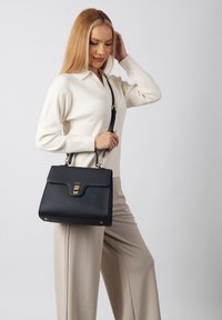 Black leather handbag with a structured design, gold-tone hardware, and a top handle, featuring a detachable shoulder strap.
