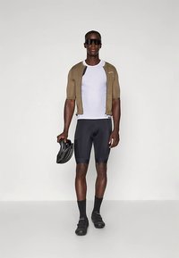 Mann iført sykkelantrekk med hvit mesh-skjorte, olivengrønn kortermet jakke, svarte sykkelshorts, svarte sko, sokker, solbriller, holder svart hjelm.