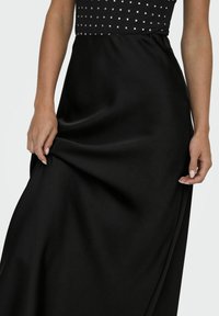 Schwarzer Satin-Maxi-Rock mit einem taillierten Oberteil und quadratischen Verzierungen. Der Rock fällt glatt und betont die weiche Textur.