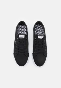 Black canvas sneakers with white rubber soles, round toes, and flat black laces. Inner lining features repeated "Pepe Jeans" logo pattern.