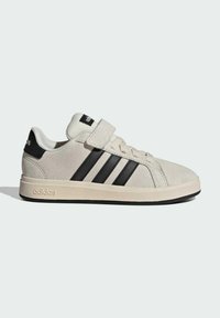 Lyse beige Adidas sneaker med sorte tre striber, velcrolukning, snørebånd og mærket hælskinne på hvid baggrund.