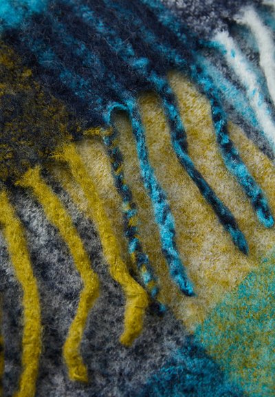 Teksturowana wełniana tkanina z niebieskimi, żółtymi i szarymi wzorami, z widocznymi frędzlami i miękkim, puszystym wykończeniem.