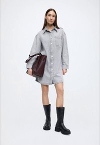 Denimskjortekjole med krave, lange ærmer, knapper foran og brystlomme. Kombineret med en bordeaux tote-taske og sorte knæhøje støvler.