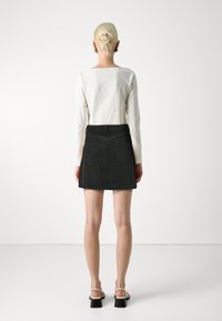 Witte lange mouwtop gecombineerd met een donkergrijs corduroy rok. Bevat achterzakken en heeft een rechte snit, gedragen met zwarte sandalen met blokhak en bandjes.