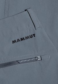Grau Stoff mit einer glatten Textur, ausgestattet mit einer Reißverschlusstasche und dem schwarzen "MAMMUT"-Logo. Die Nähte sind entlang der Kanten sichtbar.
