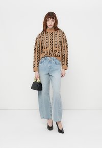 Brunmønstret strikkegenser med svarte design, lys blå vide jeans, svarte hæler og en liten svart håndveske med gullakcenter.