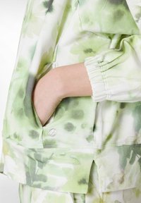 Blomstret sweatshirt i blødt stof; har pastelfarver i grøn og hvid, ribbet manchetter og en sidelomme med logo.