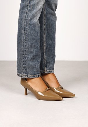 Escarpins en cuir verni marron clair avec un bout pointu et un petit talon. Dotés d'une boucle décorative à l'avant et portés avec un jean bleu.