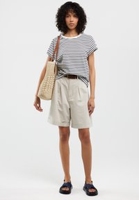 Baltos ir tamsiai mėlynos dryžuotos trumpomis rankovėmis marškiniai, kreminiai plisavimo šortai ir audinėta rankinė. Modelis dėvi tamsiai mėlynas šlepetes. Neutralus fonas.