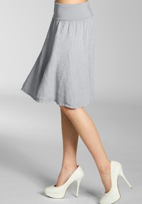 Grauer, knielanger Rock aus leichtem Stoff, mit breitem Bund und fließendem, ausgestellt Design. Kombiniert mit weißen High Heels.