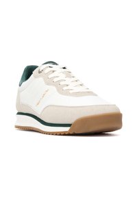 Zapatilla blanca con acentos verdes, materiales de ante y cuero, diseño con cordones y suela de goma texturizada. Presenta detalle del logotipo bordado.