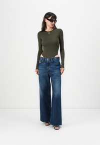 Olive green long-sleeve bodysuit paired with loose-fit dark blue jeans, featuring a high waist and wide legs, complemented by black heeled sandals.