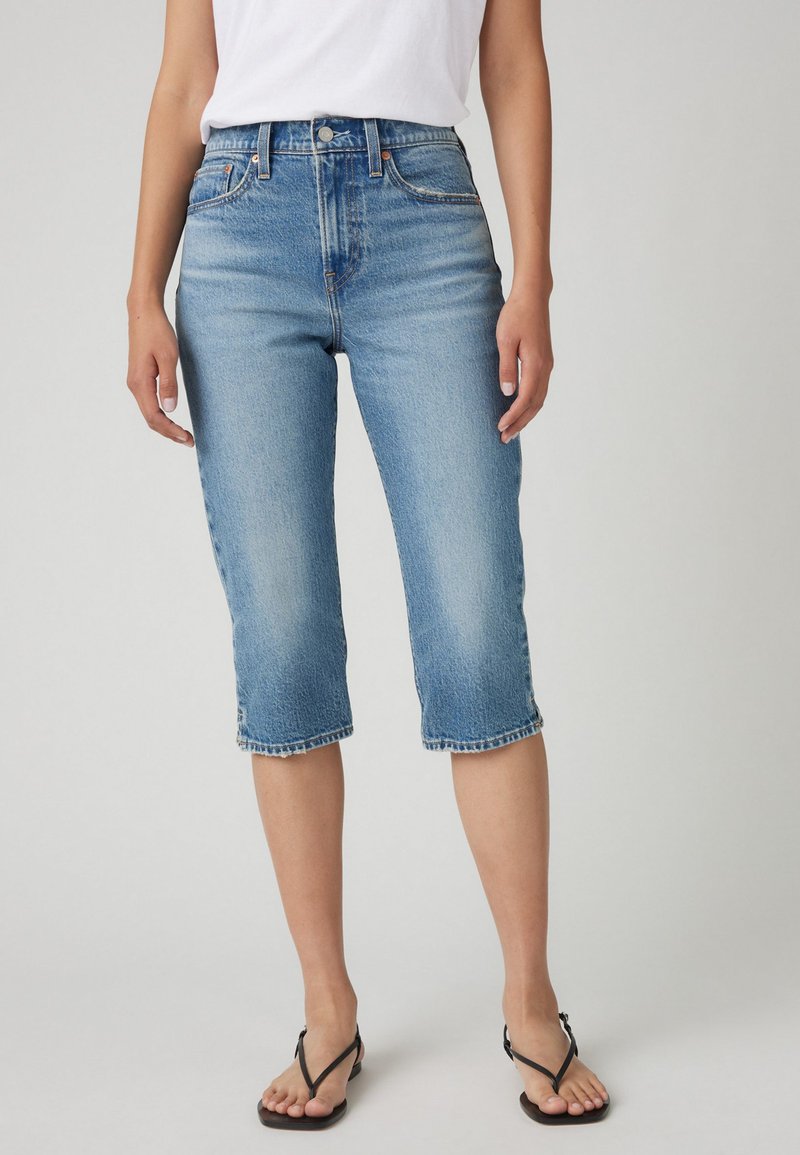 Pantalons capri en denim bleu clair avec une taille ajustée, coupe légèrement décontractée, et un ourlet qui se termine juste en dessous du genou, dotés d'un design classique à cinq poches.