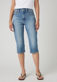 Svijetloplave traper capri hlače s uskim strukom, malo opuštenog kroja, i rubom koji završava neposredno ispod koljena, s klasičnim petodžepnim dizajnom.