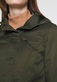 Kurtka oliwkowo-zielona z zamkiem błyskawicznym i zapięciem na zatrzaski, z kapturem i małą kieszenią na piersi zapinaną na zamek. Gładka faktura i dopasowany krój.