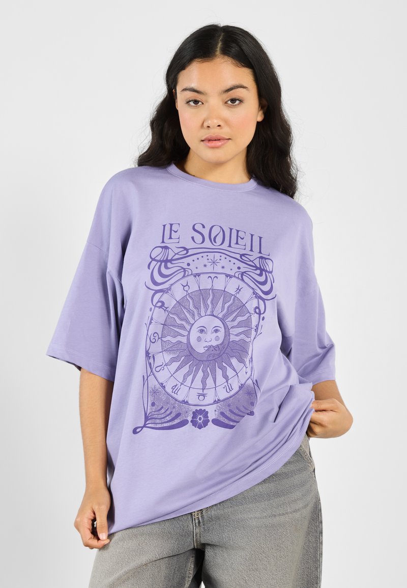 Lavender oversized t-shirt with a round neck, featuring a purple sun graphic and astrology symbols. Made from soft cotton fabric.
