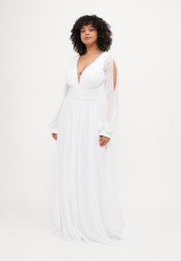 Weißes langes Kleid mit tiefem V-Ausschnitt und gerafftem Oberteil. Schwingende, durchsichtige Ballonärmel mit Ausschnittdetails. Leichter Stoff mit glatter Oberfläche.