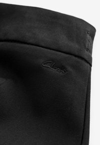 Gros plan d’un tissu noir avec le nom de la marque "Clarks" brodé près d’une couture.