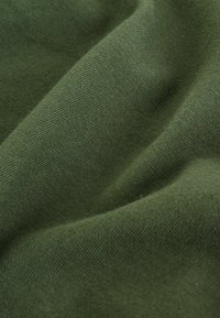 Groene katoenstof met een gladde textuur en subtiel breipatroon, die valt om diepte en contouren in de plooien te onthullen.