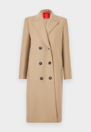 Dviejų sagų smėlio spalvos paltas su apykakle, pagamintas iš austos medžiagos. Puoštas juodais mygtukais ir lygiu paviršiumi. Vidus pamuštas ryškiai raudona medžiaga.