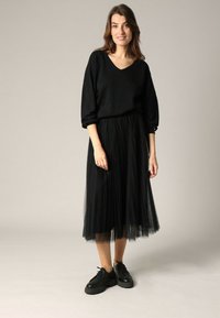 Pull noir avec une finition texturée, décolleté en V et manches amples. Associé à une jupe midi en tulle plissé noire et des chaussures lacées noires.