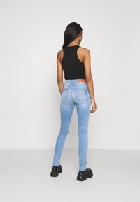 Blå denim skinny jeans med en ljus tvätt, med en brun läderlapp baktill, i kombination med en svart ärmlös topp och svarta stövlar.