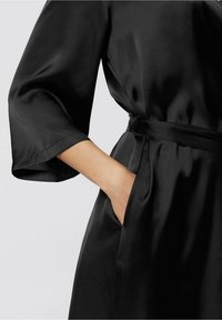 Svart satinrock med vida ärmar, knytbälte i midjan och sidofickor. Slät textur med glansig yta.