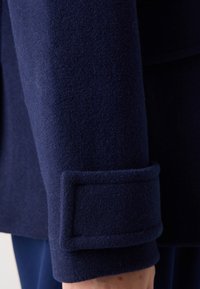 Manga de abrigo de lana azul marino con una textura suave, que presenta un puño rectangular y un acabado de costura limpio.