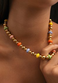 Collar de cuentas colorido que presenta cuentas esféricas doradas brillantes y acentos redondos de cerámica multicolores en rosa, verde, naranja, amarillo y azul.