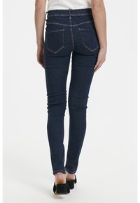 Jeans skinny azul oscuro con cintura alta, que cuentan con bolsillos cosidos y un sutil desvanecimiento. La tela parece suave y elástica.