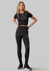 Top atletico corto nero e leggings a vita alta con un design texturizzato. Abbigliamento abbinato a scarpe da ginnastica nere, adatto per l'abbigliamento sportivo.