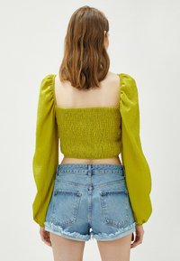 Limegrøn, cropped bluse med struktureret smock, lange pufærmer, parret med lyse denim shorts med frynset kant og lommer.