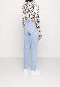 Ljusblå hög midja jeans i denim, med avslappnad passform. Blommig långärmad skjorta med ett mönster i svart och kräm. Vita sneakers.