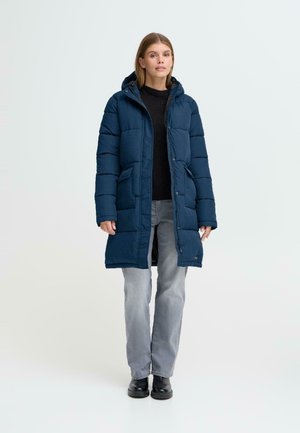 Polstret navy blue lang frakke med hætte, der har to frontlommer, en frontlynlås og et struktureret stof, båret over en sort sweater og grå jeans.