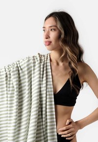 Pruhovaný zeleno-biely šál z ľahkého materiálu, prehodený cez jedno rameno. Modelka má na sebe čierny bikiny top, ktorý zobrazuje hladký povrch.