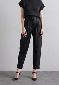 Μαύροι πλισέ παντελόνια σε συνδυασμό με ένα σκούρο πλεκτό τοπ, με ψηλό μέσο και ζώνη, συμπληρωμένα από μαύρες ψηλοτάκουνες γόβες. Λείο υλικό.