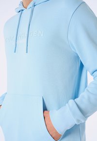 Felpa leggera blu chiaro realizzata in morbido tessuto, con tasca a marsupio, cordino regolabile e logo "Copenhagen" in rilievo sul davanti.