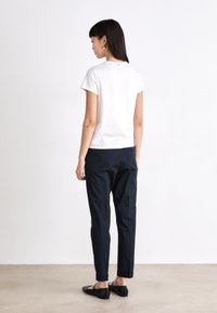 White cotton t-shirt with short sleeves, paired with navy blue tapered pants. Black flats worn on bare feet, showing a minimalistic design.