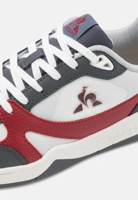 Sneaker grigio, bianco e rosso con pannelli in pelle testurizzata e mesh, lacci bianchi piatti, accentuazione del logo sul lato, suola imbottita.