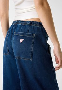 Denim spordipüksid elastse vöökohtaga, tumeda sinise värviga, kahe tagataskuga ja kolmnurkse logopatch'iga paremal taskul.