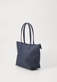 Navy tote bag with textured material, two long handles, and a zip closure. Minimalist design with a structured shape and no visible hardware.