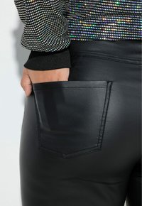 Zwarte neplederen broek met een achterzak, gecombineerd met een zwarte pailletten-top met veelkleurige, reflecterende stippen en elastische boorden.