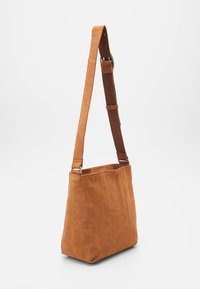 Brązowa zamszowa torba na ramię o płaskim kształcie, z regulowanym paskiem i pionowymi szwami. Charakteryzuje się gładką fakturą i minimalistycznym designem.