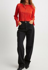 Czerwony, plisowany crop top z długim rękawem i falbankami na mankietach, zestawiony z czarnymi, wysokogatunkowymi dżinsowymi spodniami o szerokich nogawkach i czarnymi, spiczastymi botkami.