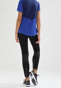 Blå idrottströja med en mörkblå panel, tillsammans med svarta leggings med nätinslag och dragkedjor vid anklarna, och svarta sneakers.