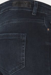 Donkerblauwe spijkerbroek met een achterzak, subtiele stikdetails en een zwart stoffen label met "ONLY" op de tailleband.