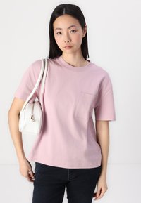 Różowa koszulka bawełniana z krótkimi rękawami i kieszonką na piersi, w połączeniu z białą torbą na zamek o zaokrąglonym kształcie.