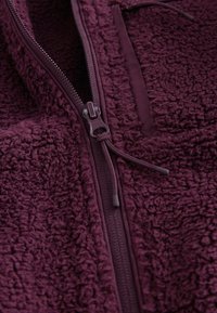 Bordeauxfarvet fleecejakke med tekstureret overflade og glat indvendig foring, med lynlåslukning og justerbar snøre.
